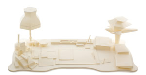 Precise three-dimensional paper reconstruction of a workspace by Herbert Stattler, showing desk objects as monochromatic white paper models based on original pencil drawings.